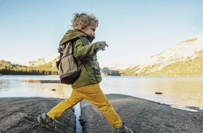 child in outdoor gear jumping over large stones in a river