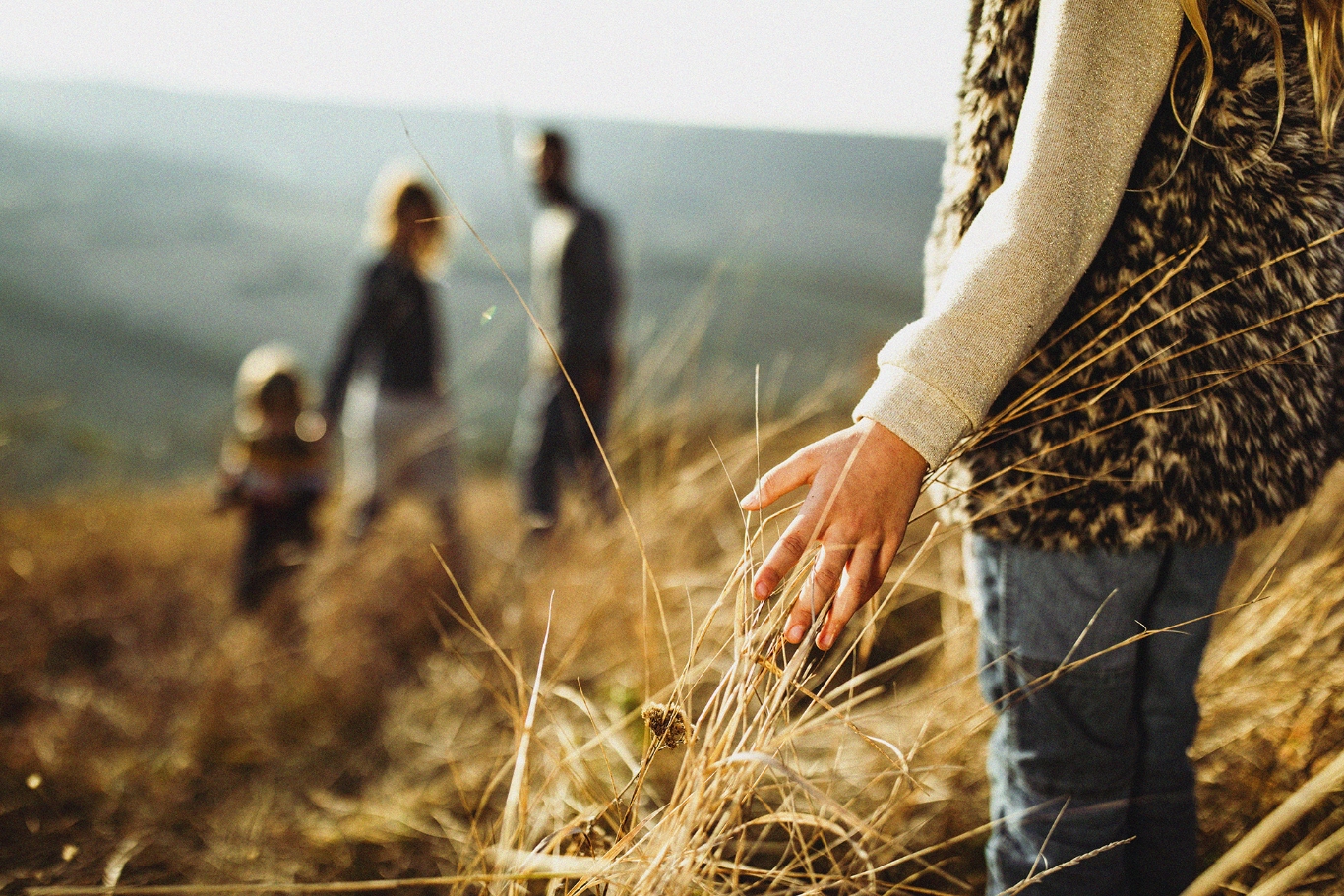 woman running her hands through the grass during a walk through the trails with family