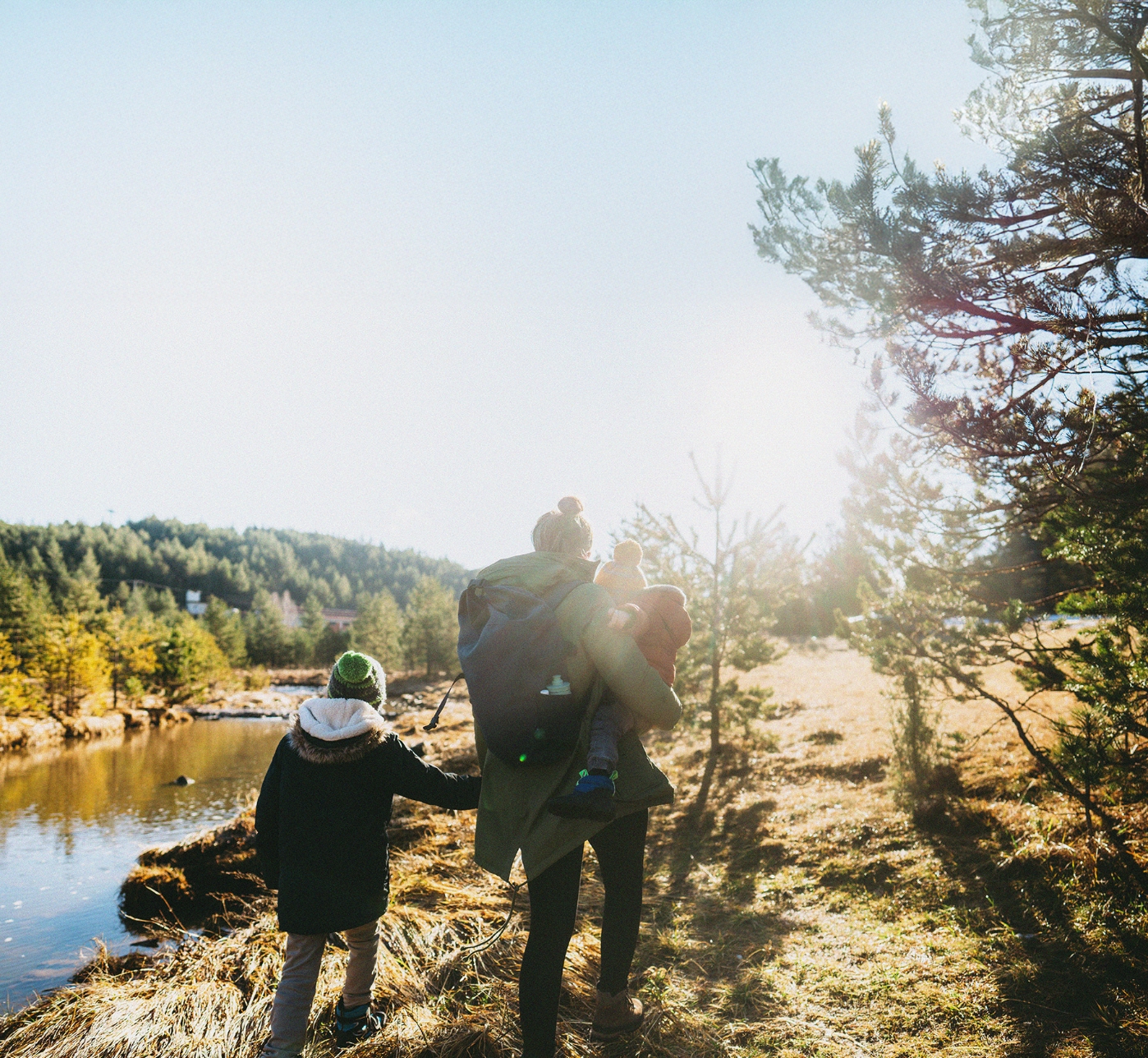 mother holding a baby and a small child's hand walking along a path next to a creek in the fall