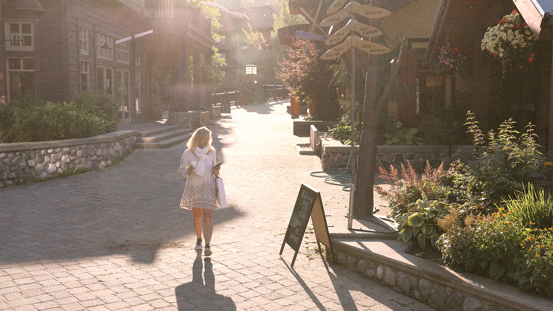 Woman walks around a brick path in a mountain shopping center with coffee - Big Sky Quarry's commercial space