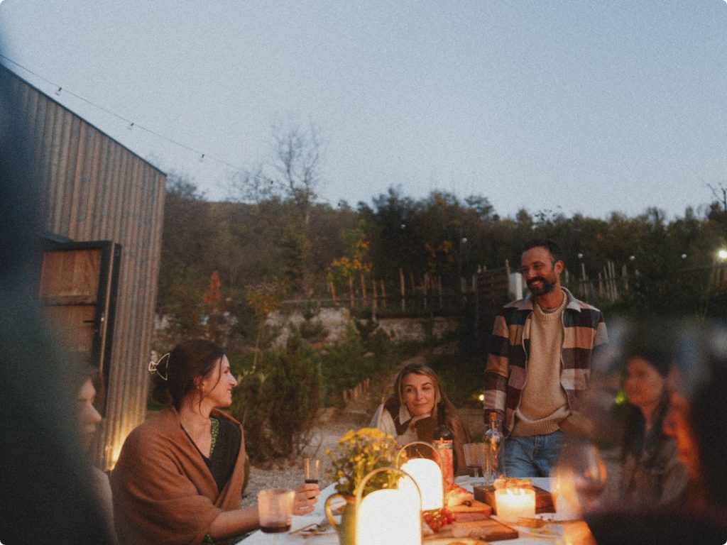 friends sitting outside around a table having food and drinks at sunset, surrounded by trees