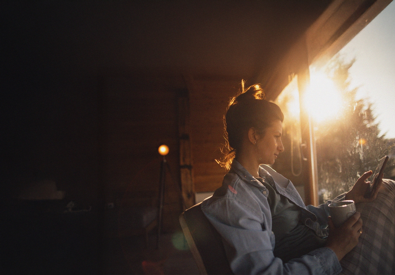 woman sitting on a rustic porch with her coffee at sunrise looking at her phone