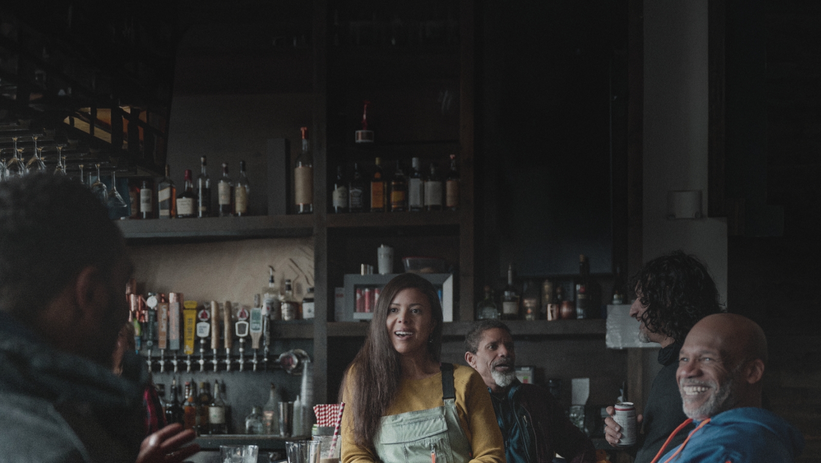 friends talk around a table with food and drinks, smiling in an industrial bar