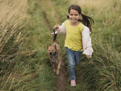 little girl holding a dog leash running and smiling along a grassy path