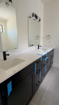 Bathroom vanity in a new Big Sky Quarry home with black cabinetry, light-colored countertops, matte black faucets, and large wall mirrors.