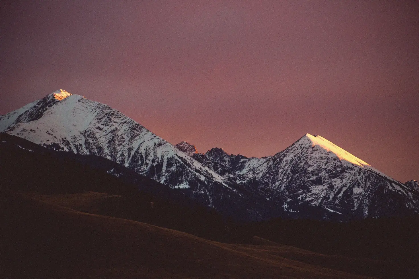 snow capped mountain range with a purple magenta sky at night